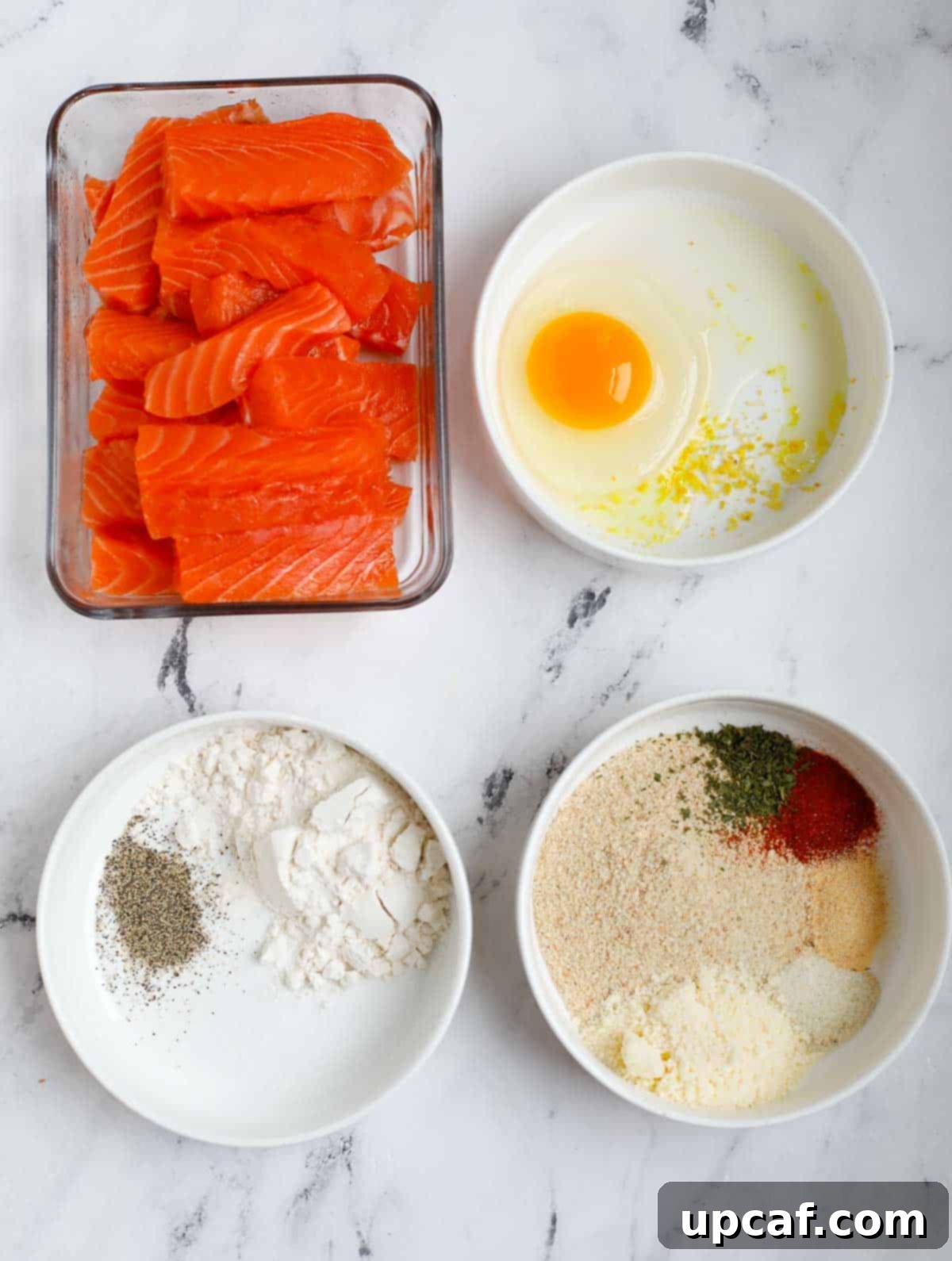 Ingredients needed for crispy salmon fish fingers, laid out on a white surface.