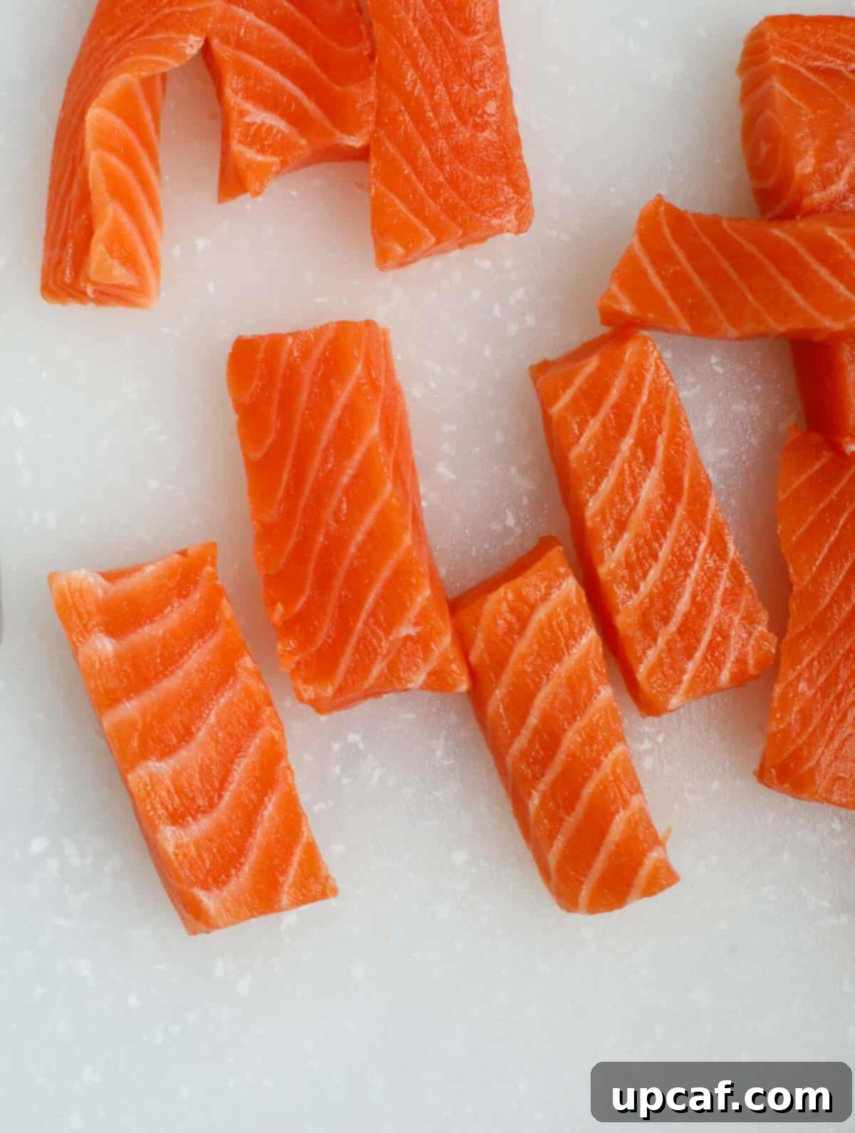 Salmon fillet being cut into fish stick shapes on a cutting board.