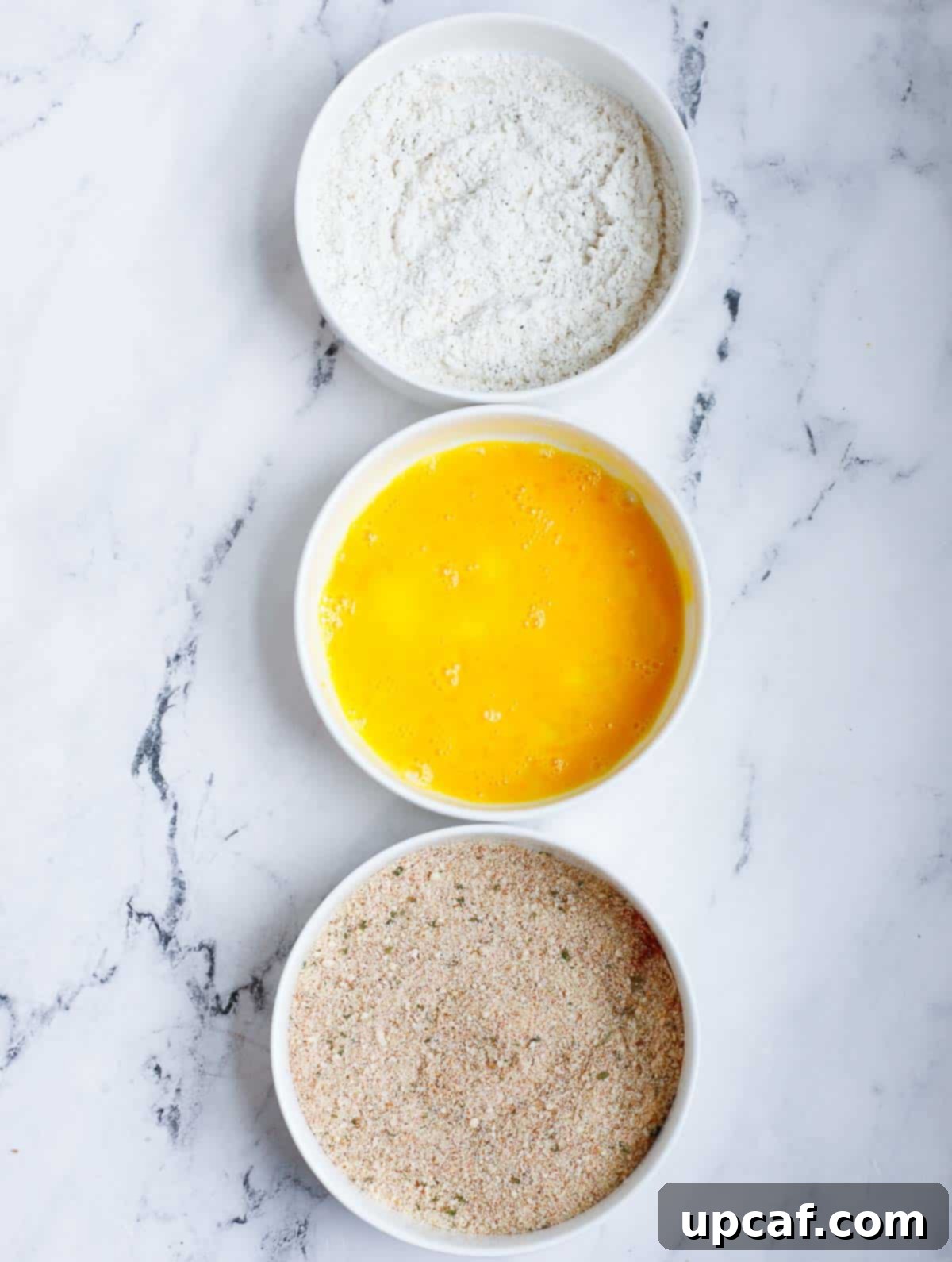 Three bowls showing the flour mixture, egg wash, and panko mixture for breading salmon.