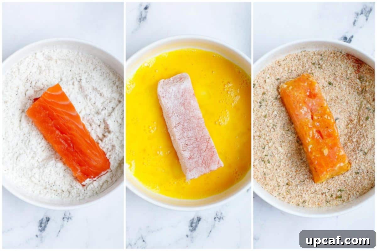 A hand coating a salmon stick with panko breadcrumbs.