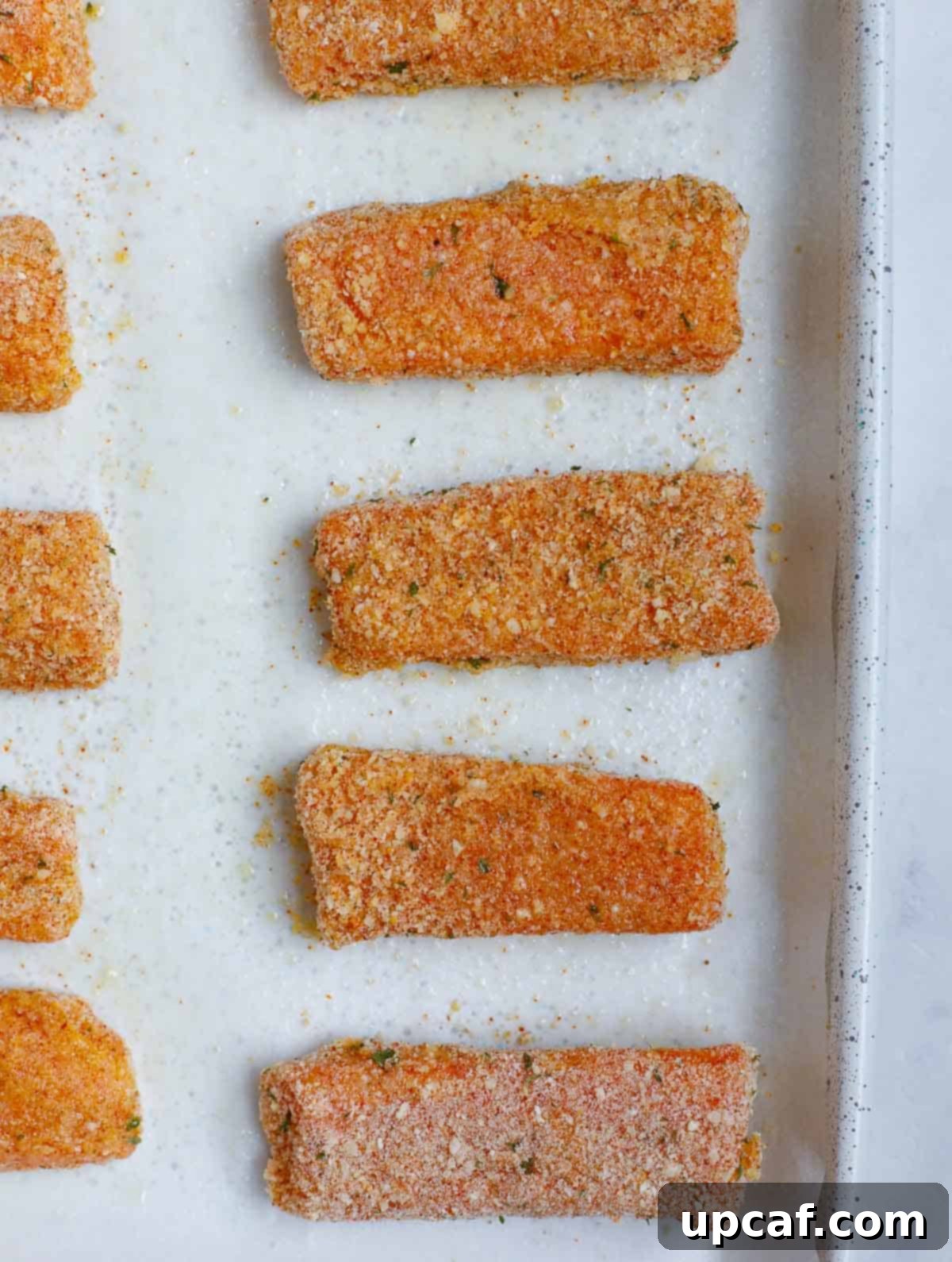 Breaded salmon fish sticks arranged on a baking tray, ready for the oven.
