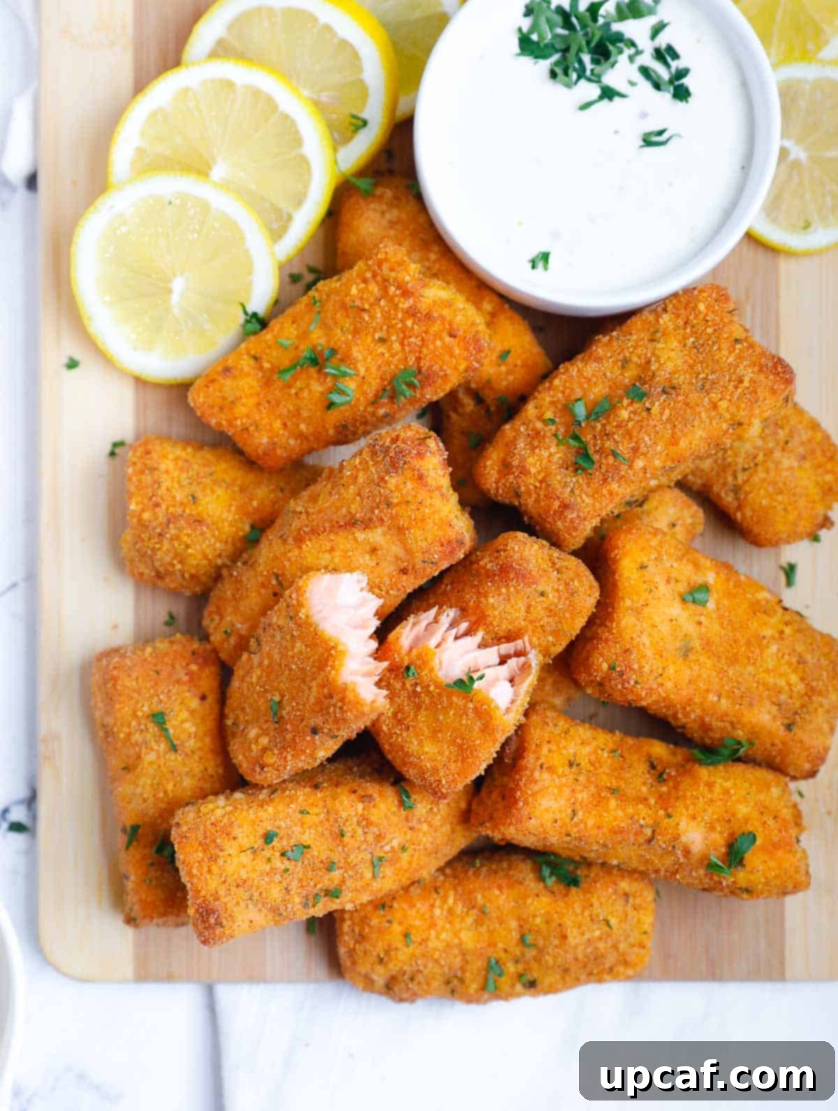 Crispy baked salmon fish fingers plated with dipping sauce, lemon wedges, and fresh parsley.