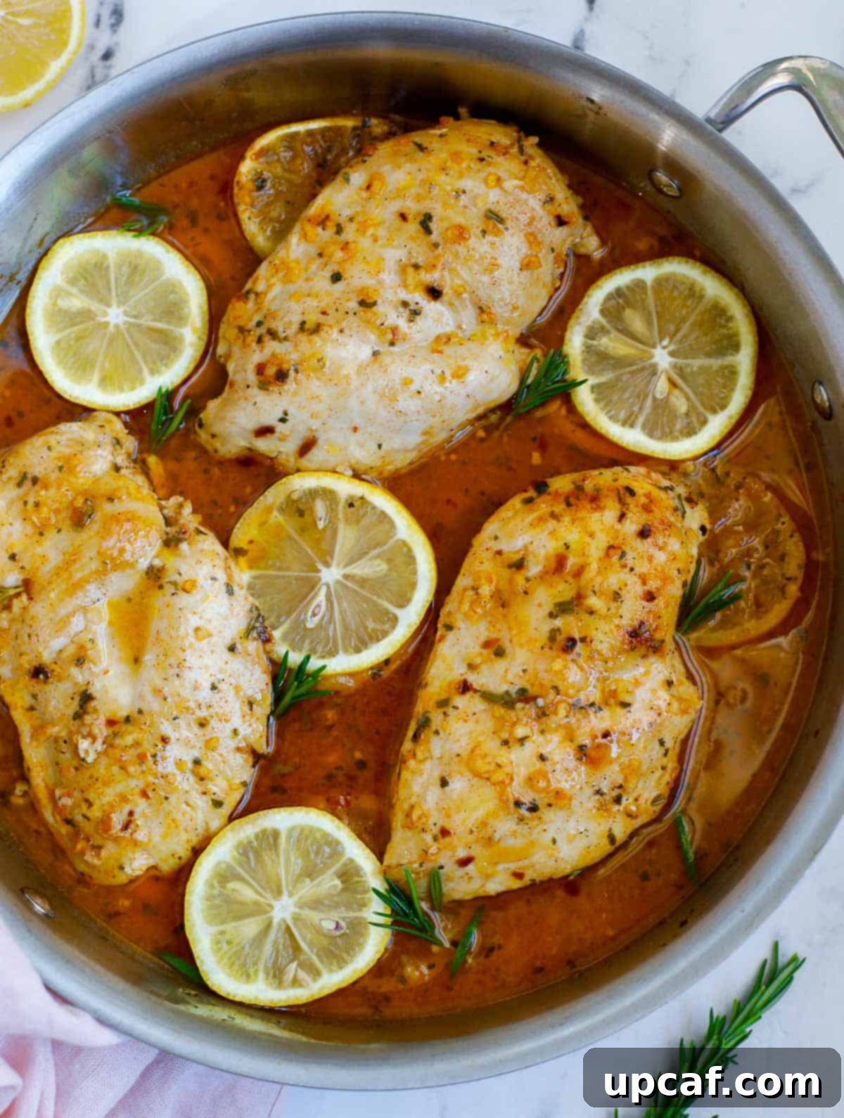 Bright Lemon Rosemary Chicken 2 Golden-brown rosemary lemon chicken breasts sizzling in a skillet, garnished with fresh rosemary and lemon slices.