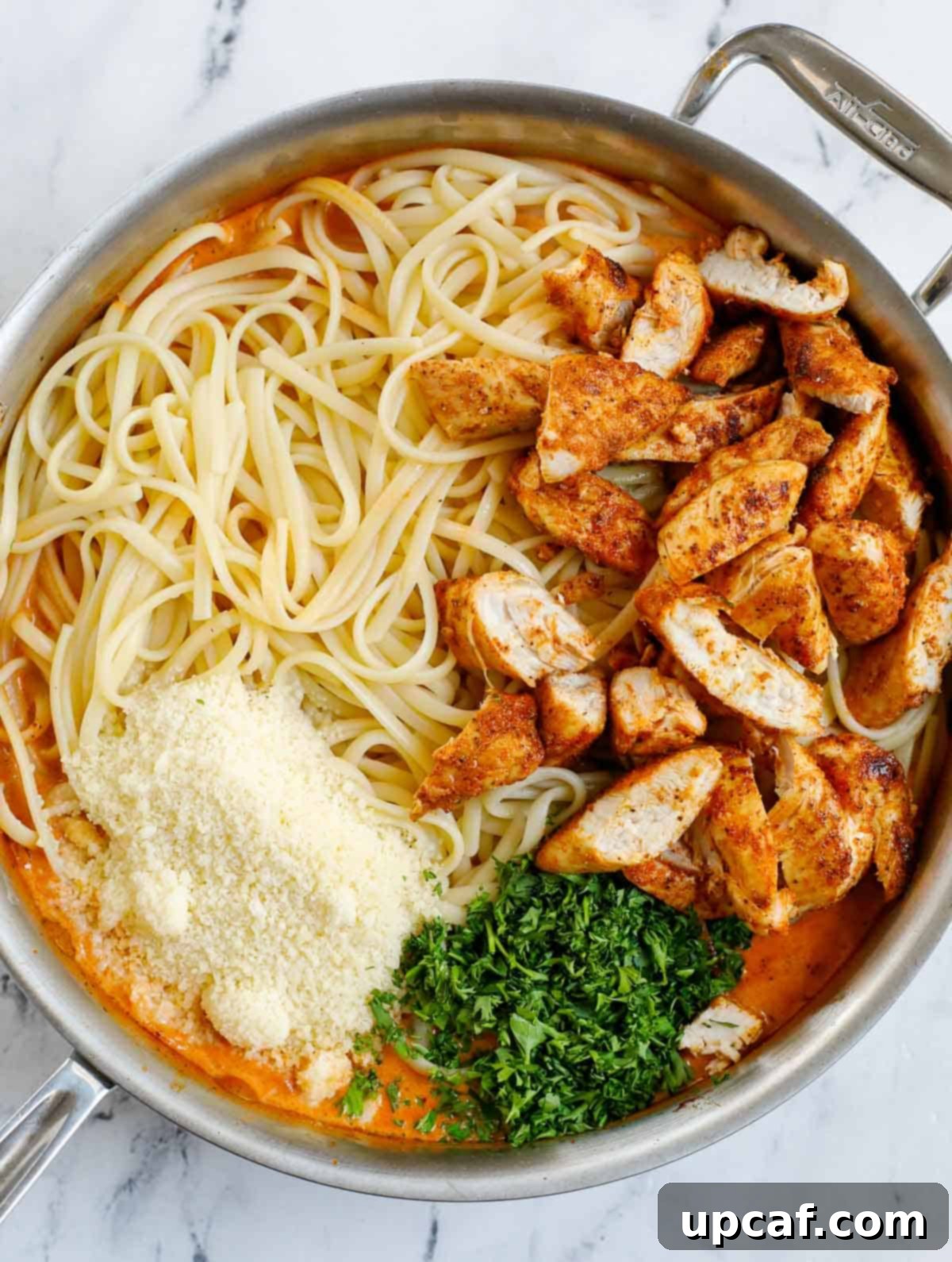 Combining cooked pasta and cubed chicken with spicy pasta sauce in a skillet.