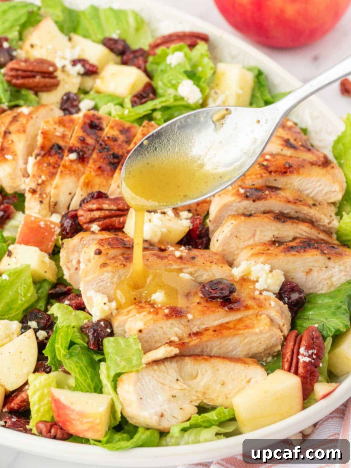 Fall Harvest Chopped Chicken Salad 8 A close-up shot of a spoon drizzling maple dressing over the freshly mixed autumn chopped chicken salad.
