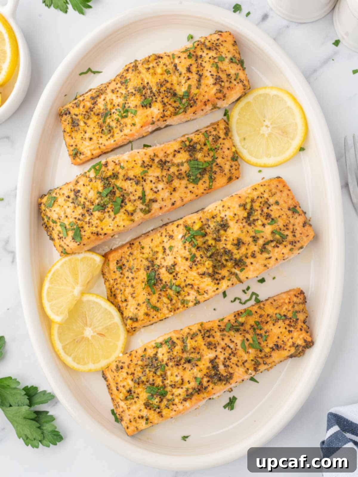 Zesty Lemon Pepper Salmon 2 Lemon pepper baked salmon on a platter garnished with lemon slices, ready to be served.