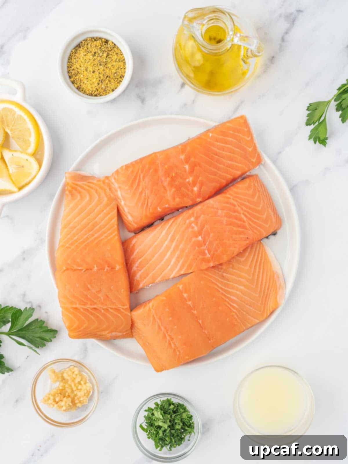 Zesty Lemon Pepper Salmon 3 Key ingredients laid out for baked lemon pepper salmon: salmon fillets, olive oil, lemon, lemon pepper seasoning, parsley, and garlic.