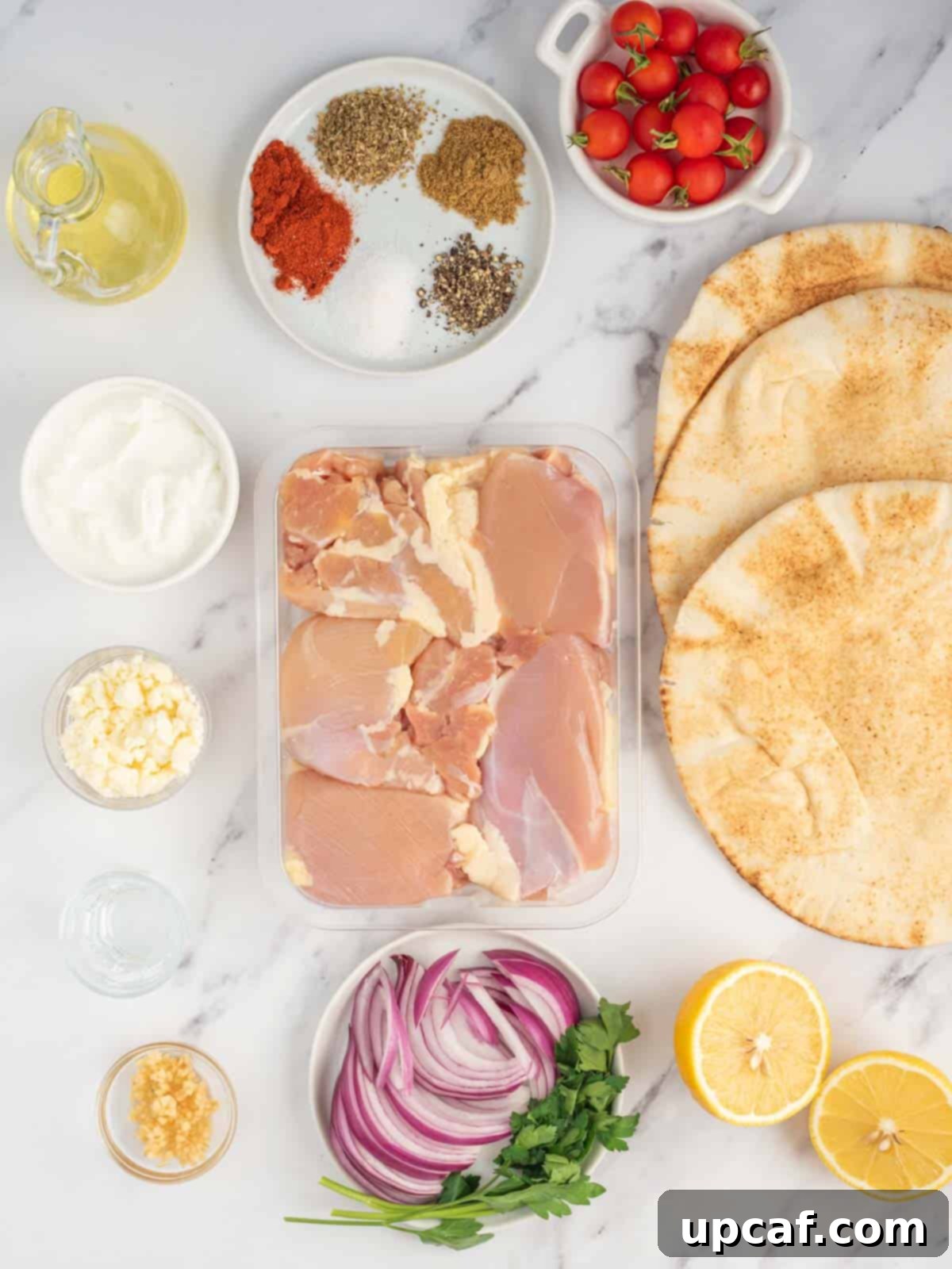 Ingredients needed for homemade greek chicken gyros, including chicken, yogurt, spices, and fresh vegetables.
