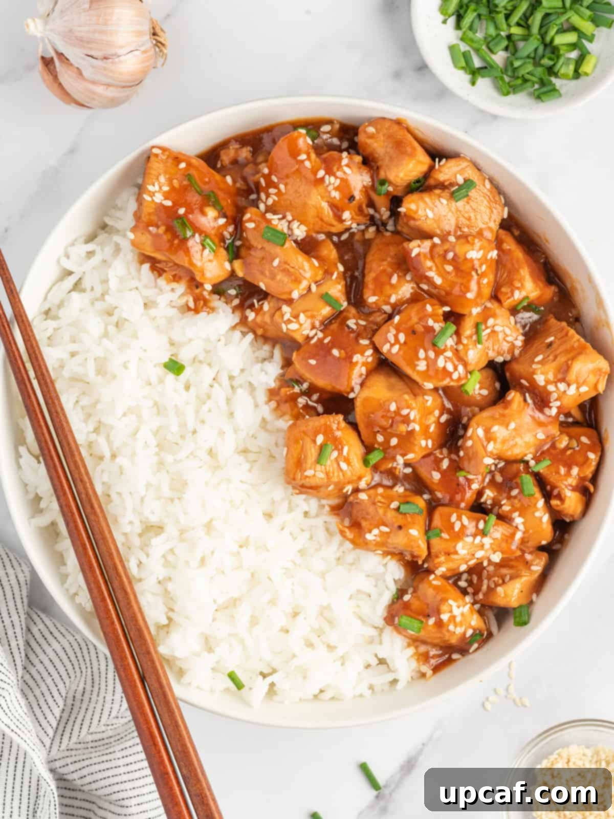 Chinese sesame chicken in a bowl with rice and chopsticks resting on the side.