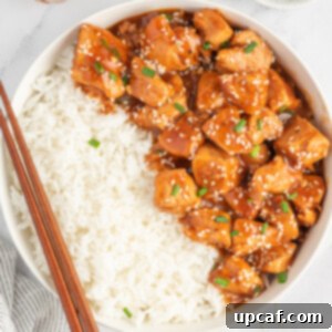 Chinese sesame chicken in a bowl with rice and chopsticks resting on the side.