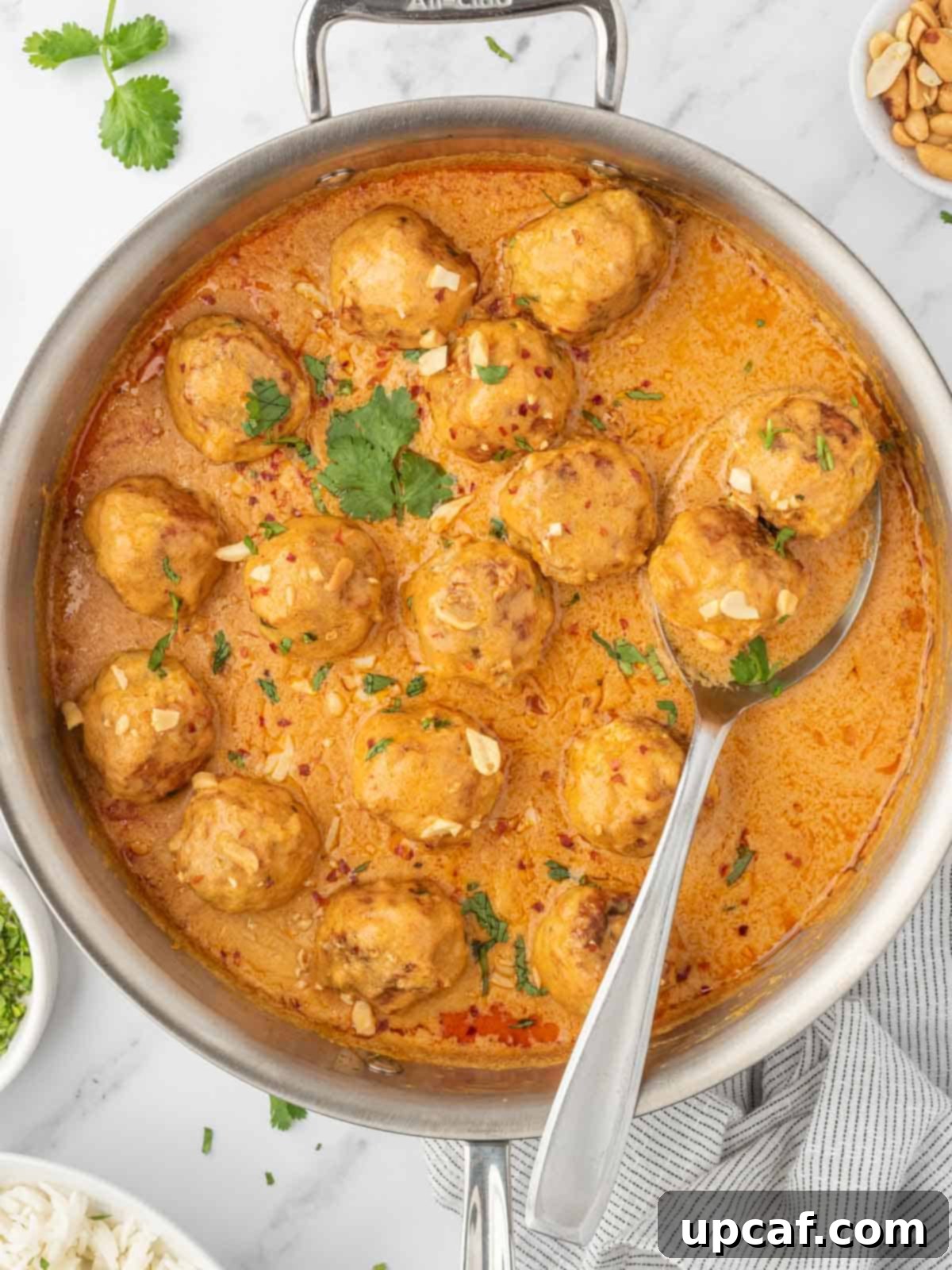 Thai Spiced Chicken Meatballs 2 Flavorful Thai Chicken Meatballs simmering in a rich coconut curry sauce in a skillet, ready to be served.