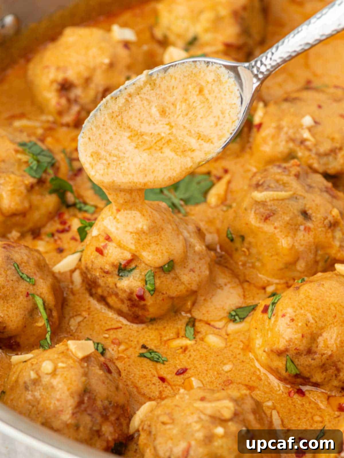 Thai Spiced Chicken Meatballs 9 A spoon drizzles rich, creamy curry sauce over a perfectly cooked Thai chicken meatball, highlighting the luscious texture of the dish.