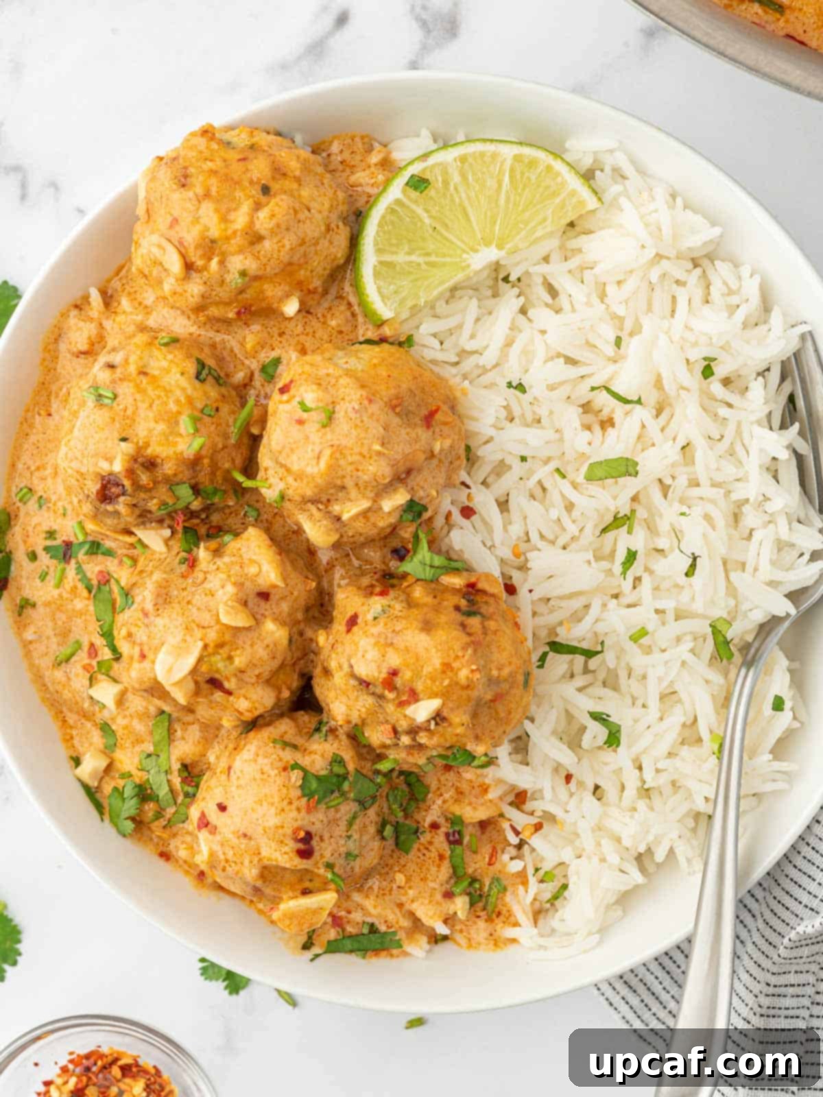 Thai Spiced Chicken Meatballs 10 A beautifully plated bowl of Thai chicken meatballs served over fluffy white rice, garnished with fresh cilantro and a lime wedge, ready to be enjoyed with a fork.