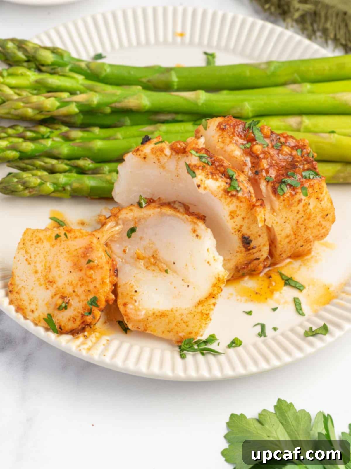 Cajun Garlic Butter Baked Cod 7 Flaked cod filets on a plate with asparagus.