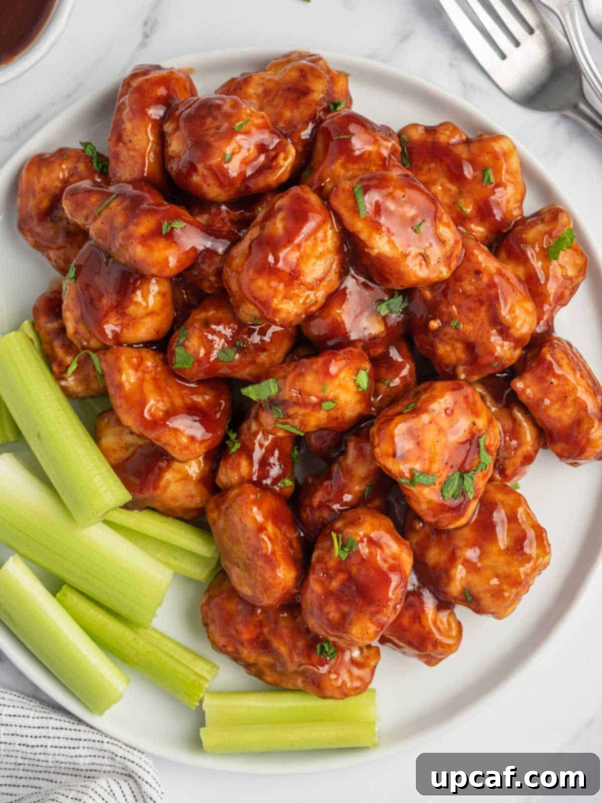 Top view of baked BBQ chicken bites with celery on a plate, showcasing a vibrant and appealing presentation.