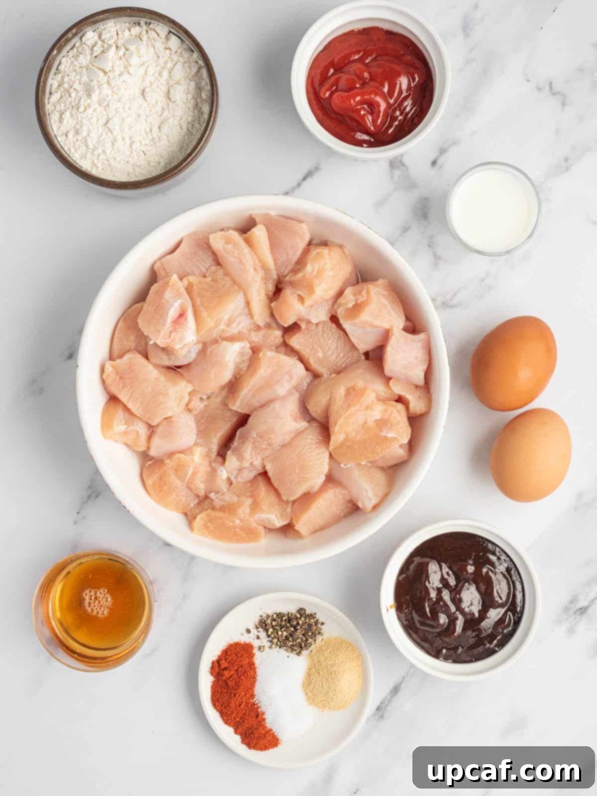 A curated display of all ingredients required for preparing baked BBQ chicken bites, neatly arranged on a white surface.