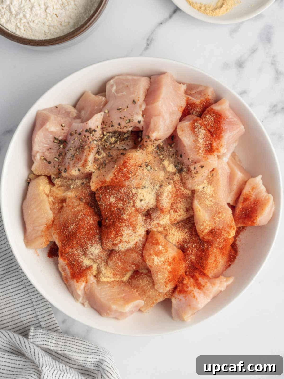 A close-up view of chicken pieces being tossed with seasoning in a bowl, showing an even coat of spices.