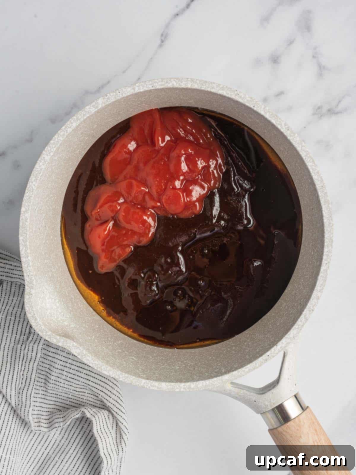 A small saucepan on a stovetop with BBQ sauce, ketchup, and honey being mixed, preparing the sweet and tangy sauce.