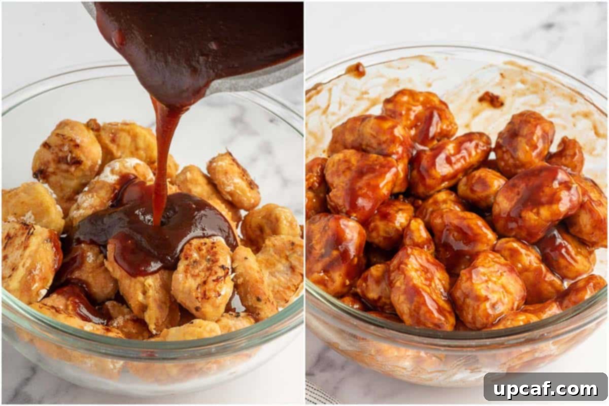 Baked chicken bites in a large bowl, with a rich, glossy BBQ sauce being poured over them, ready for tossing.