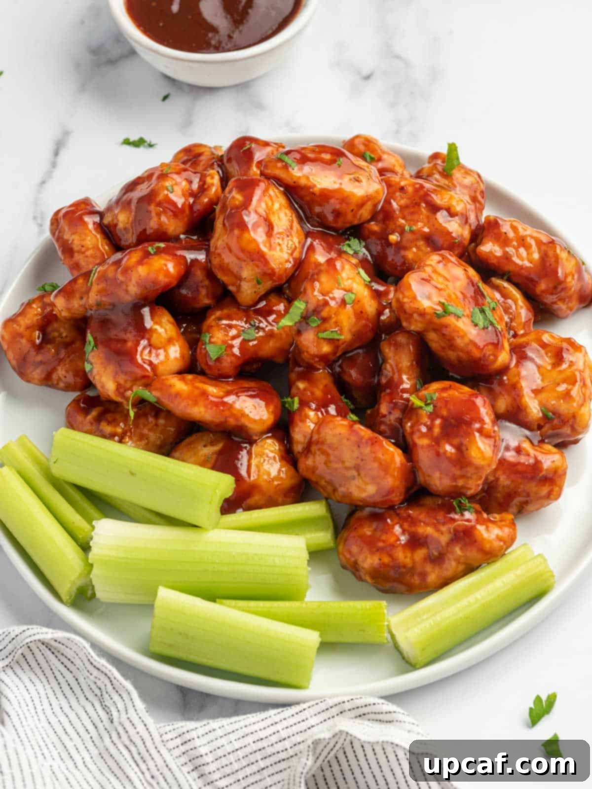 A vibrant plate of honey BBQ chicken bites, garnished with fresh parsley and served with crisp celery sticks.
