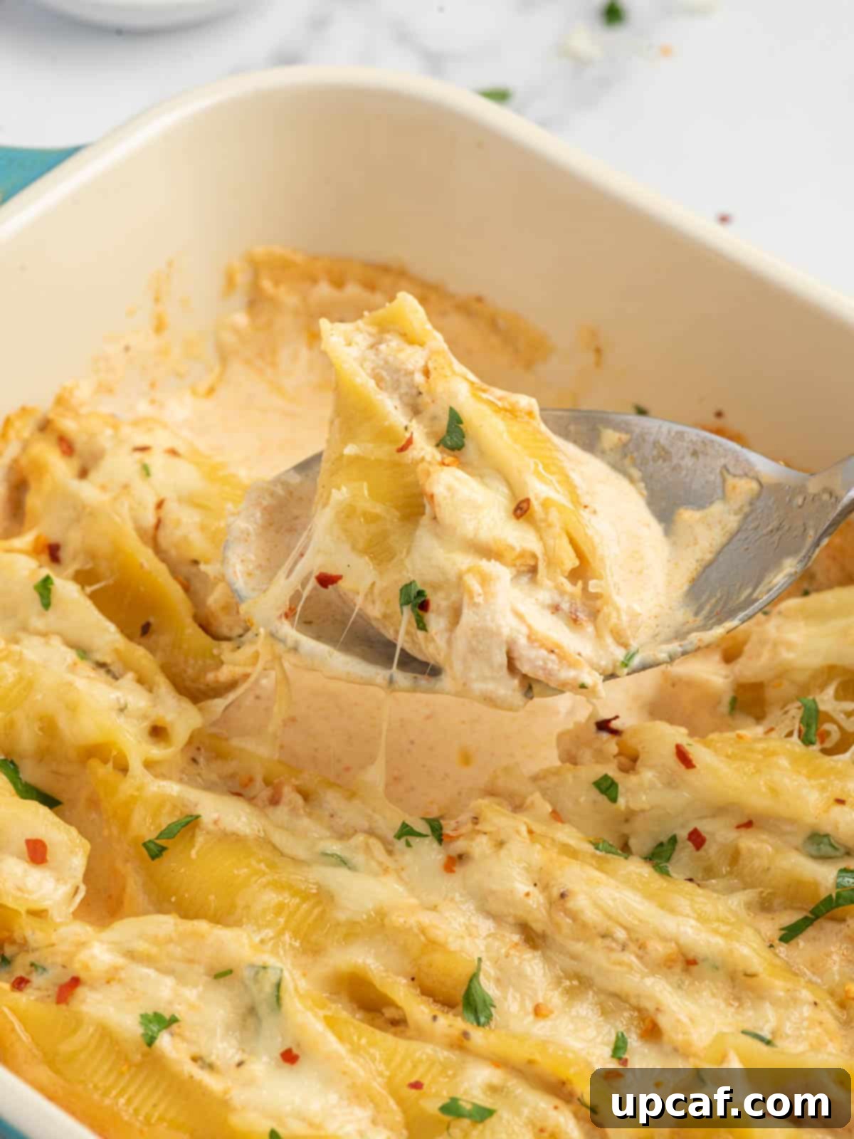 A spoon dishes out a pasta shell stuffed with cajun chicken.