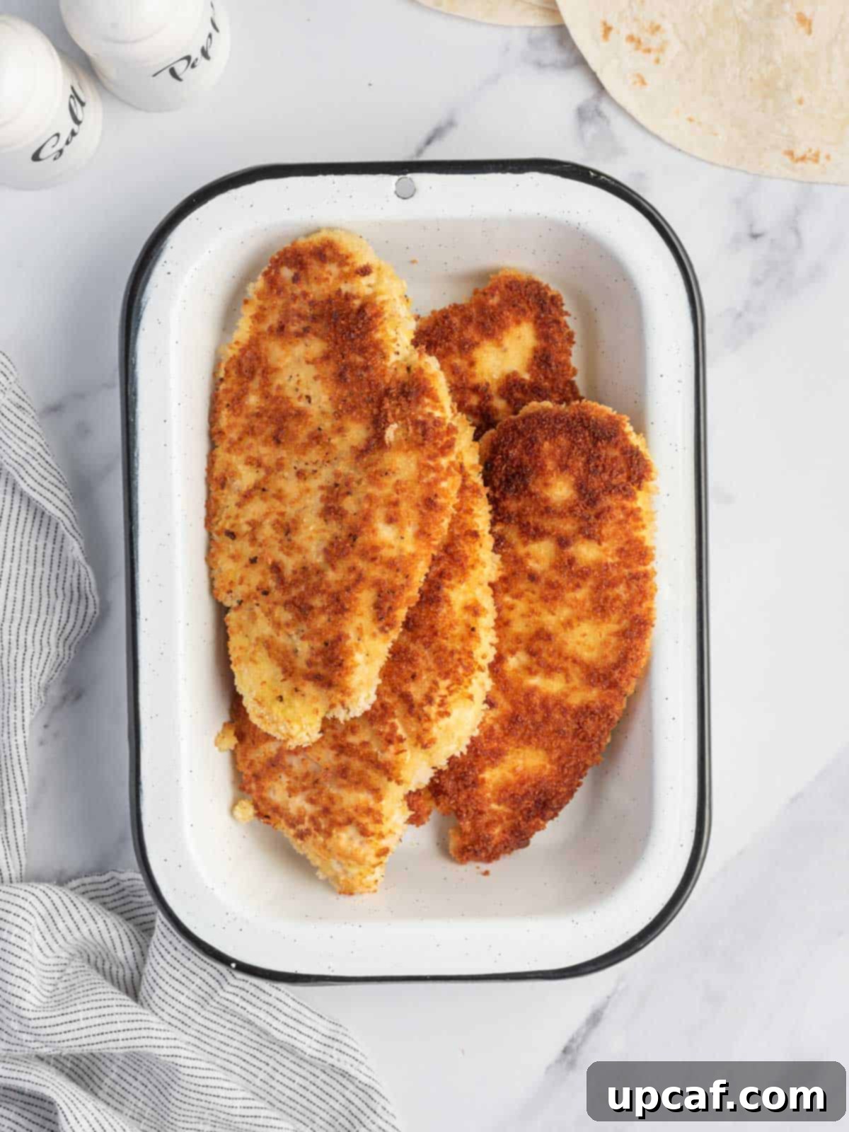 Golden-brown, homemade pan-fried chicken strips resting in a tray, perfectly cooked and ready for the next step.