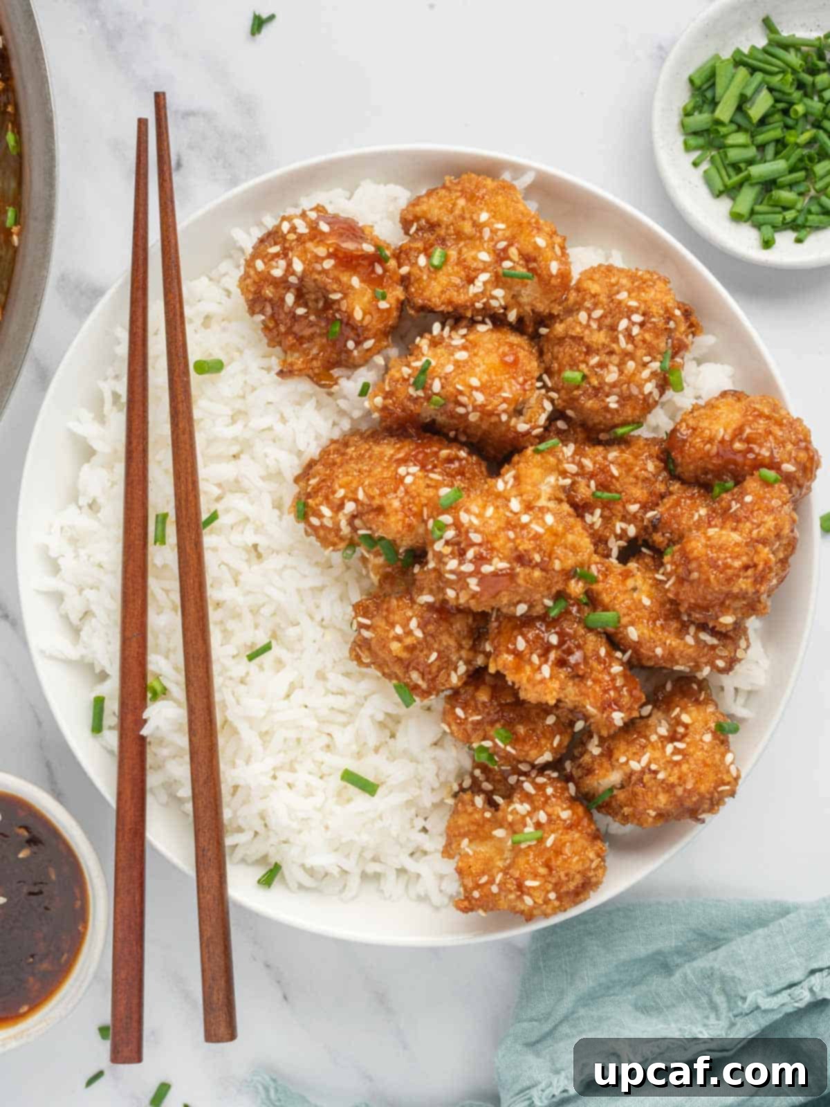 Sesame Glazed Cauliflower Poppers 2 Chop sticks rest on a bowl of rice and vegan sesame cauliflower.