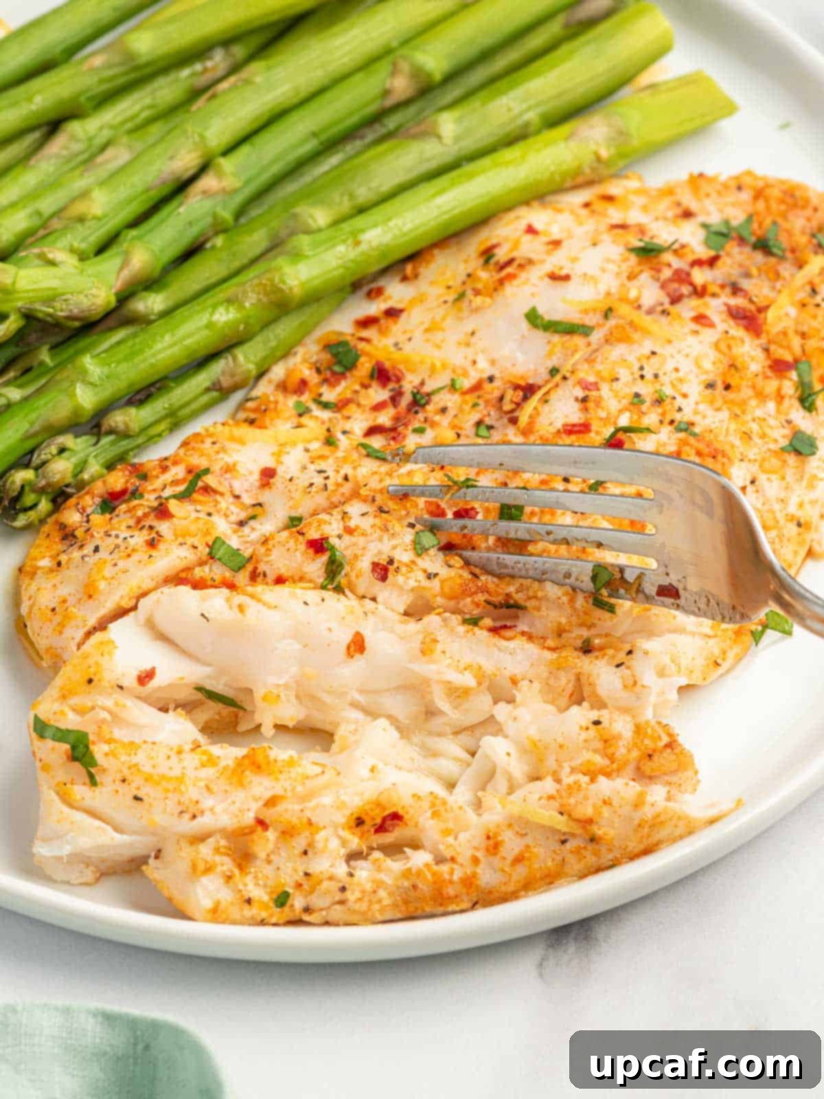 A fork flakes a garlic butter tilapia filet on a plate.