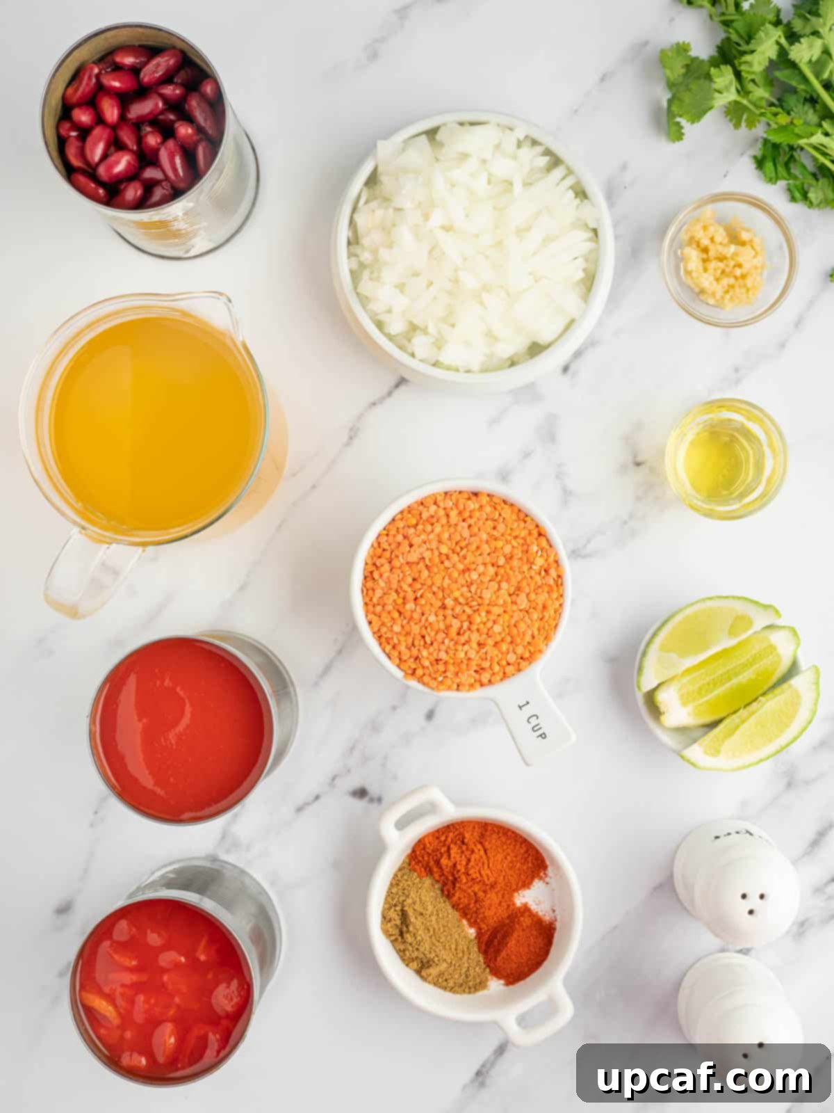 Hearty Plant-Based Lentil Chili 3 A collection of fresh ingredients laid out on a wooden board, including yellow onions, garlic, dried red lentils, a can of kidney beans, canned diced tomatoes, tomato sauce, and spices.