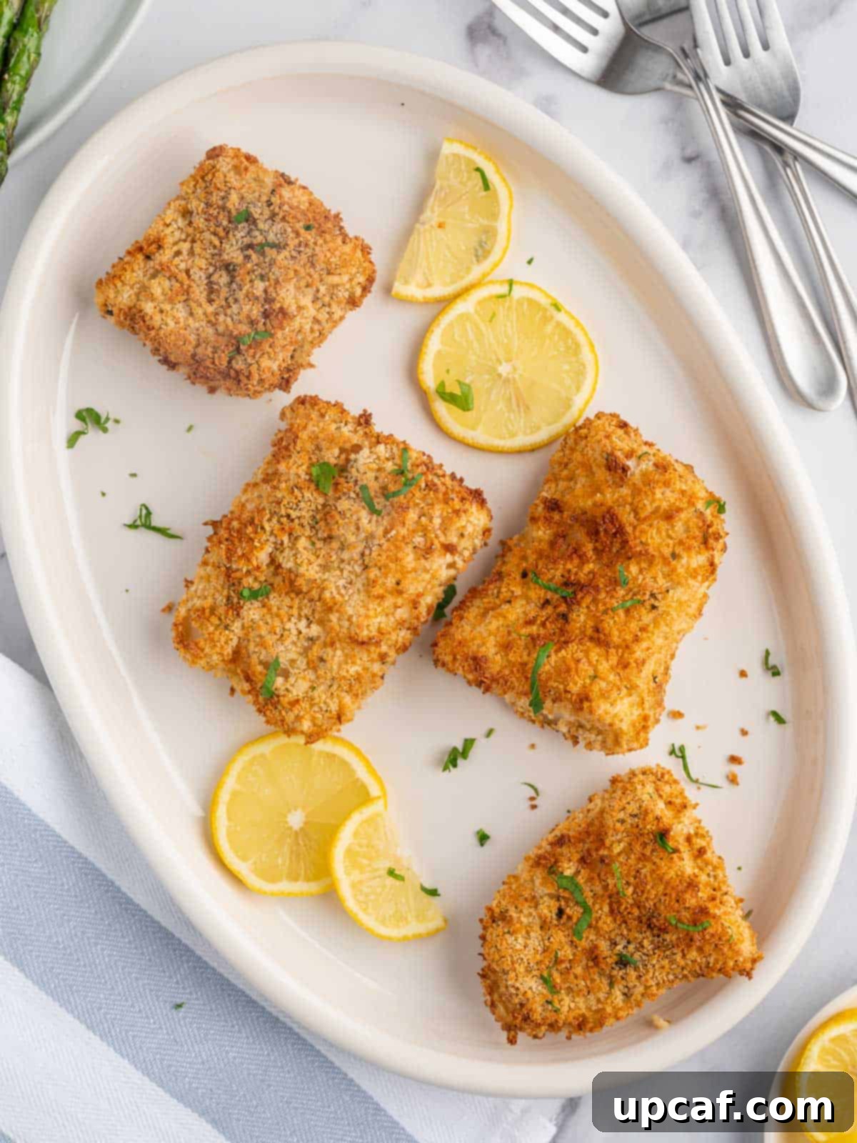 Perfectly golden-brown crispy air fryer cod fillets garnished with fresh parsley and lemon wedges.