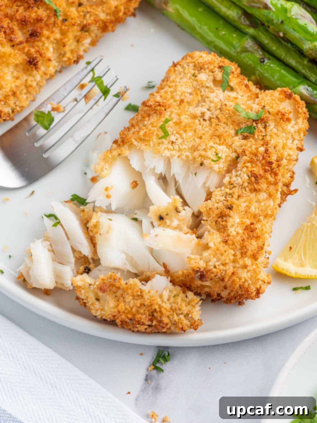 A fork flaking a piece of perfectly cooked air fried cod to show its tender, moist interior.