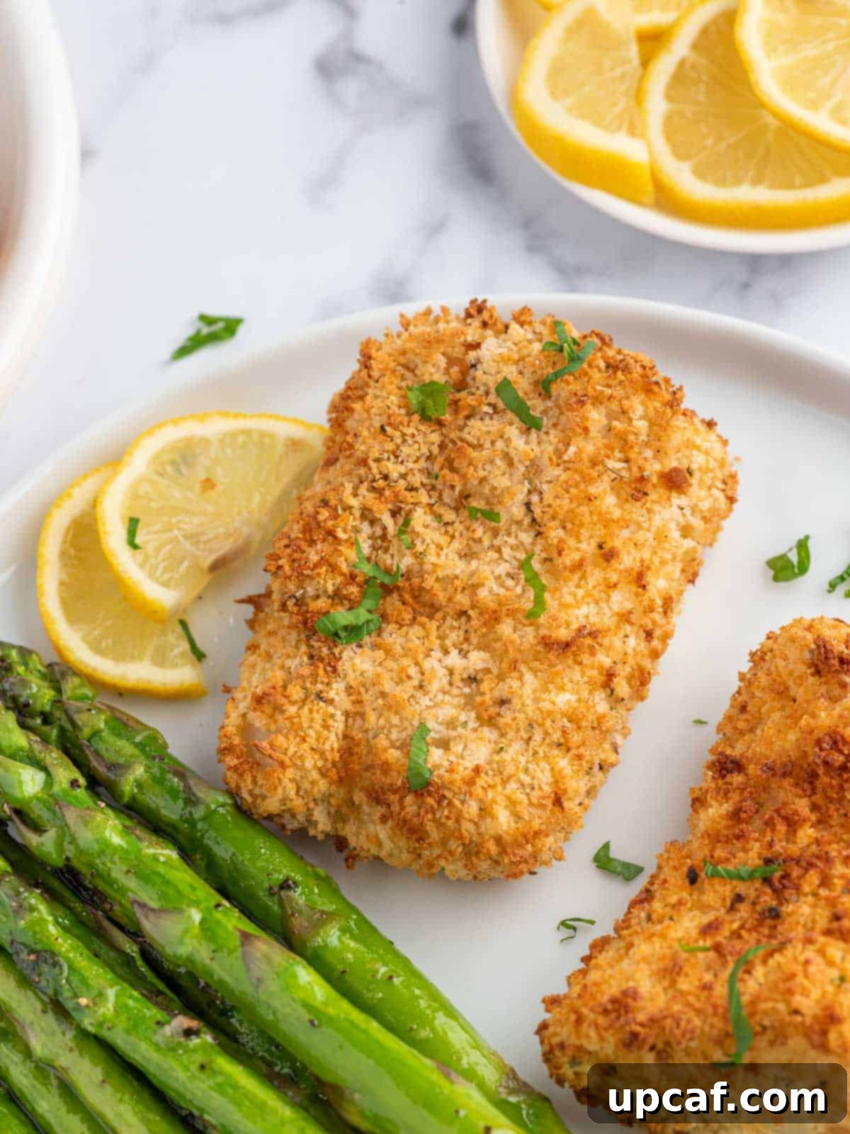 A delicious plate of panko-crusted cod served with grilled asparagus and lemon wedges.