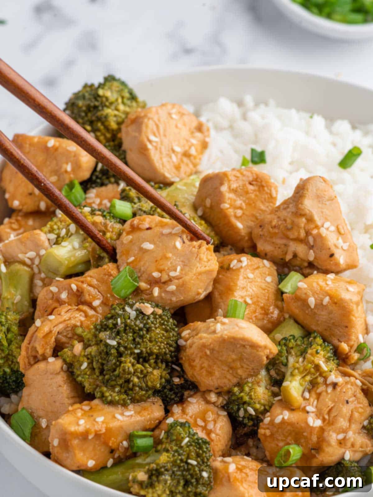 Chopsticks pick up a piece of tender chicken from a plate with rice.