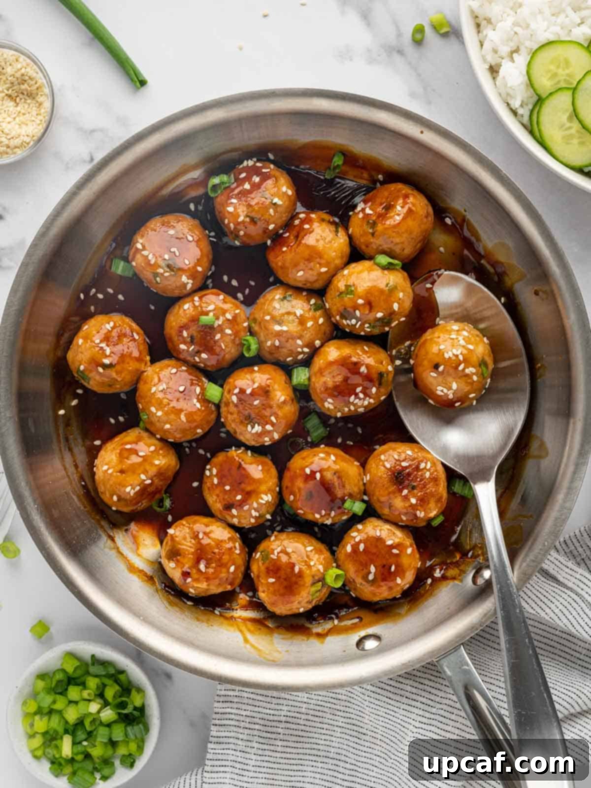 A spoon lifts a teriyaki chicken meatball from a skillet, showcasing its glossy sauce.
