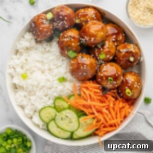 Teriyaki meatballs on a plate with rice, sliced cucumber and julienned carrots, ready to be served.