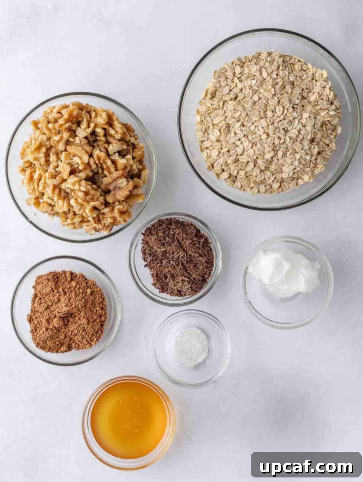 A flat lay photograph showcasing all the fresh and natural ingredients required to make homemade chocolate granola, including oats, walnuts, cocoa, and honey.