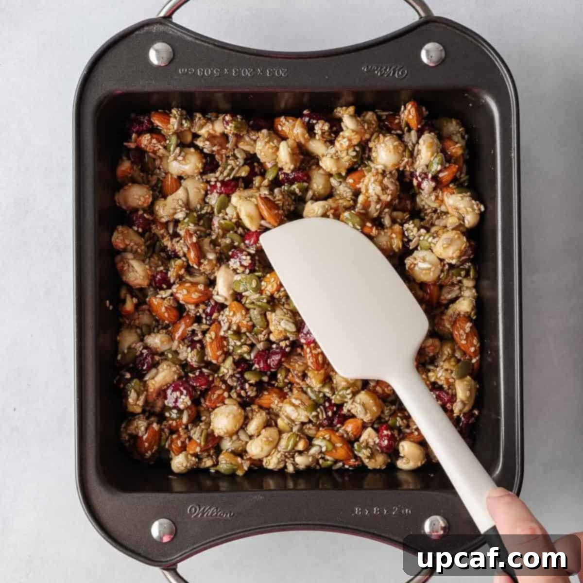 A spatula presses the healthy nut bar recipe into a pan.