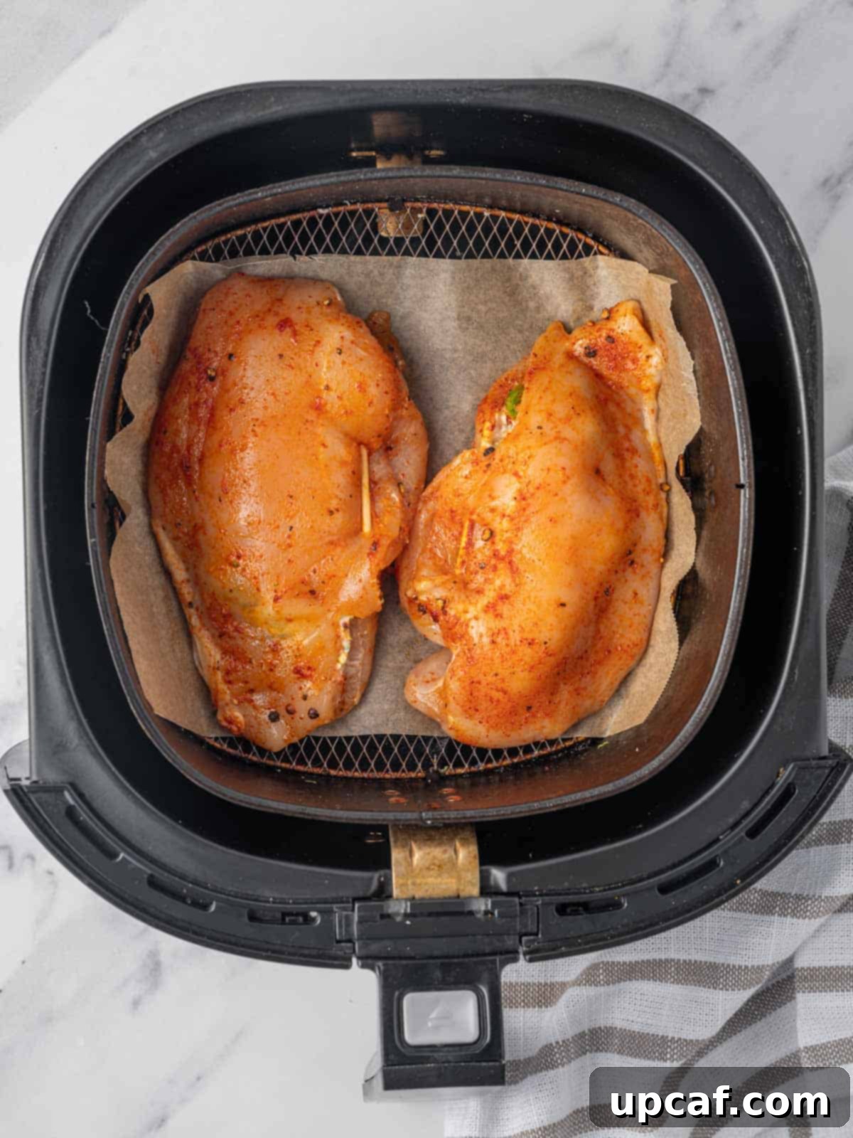 Raw stuffed chicken breast arranged in an air fryer basket.