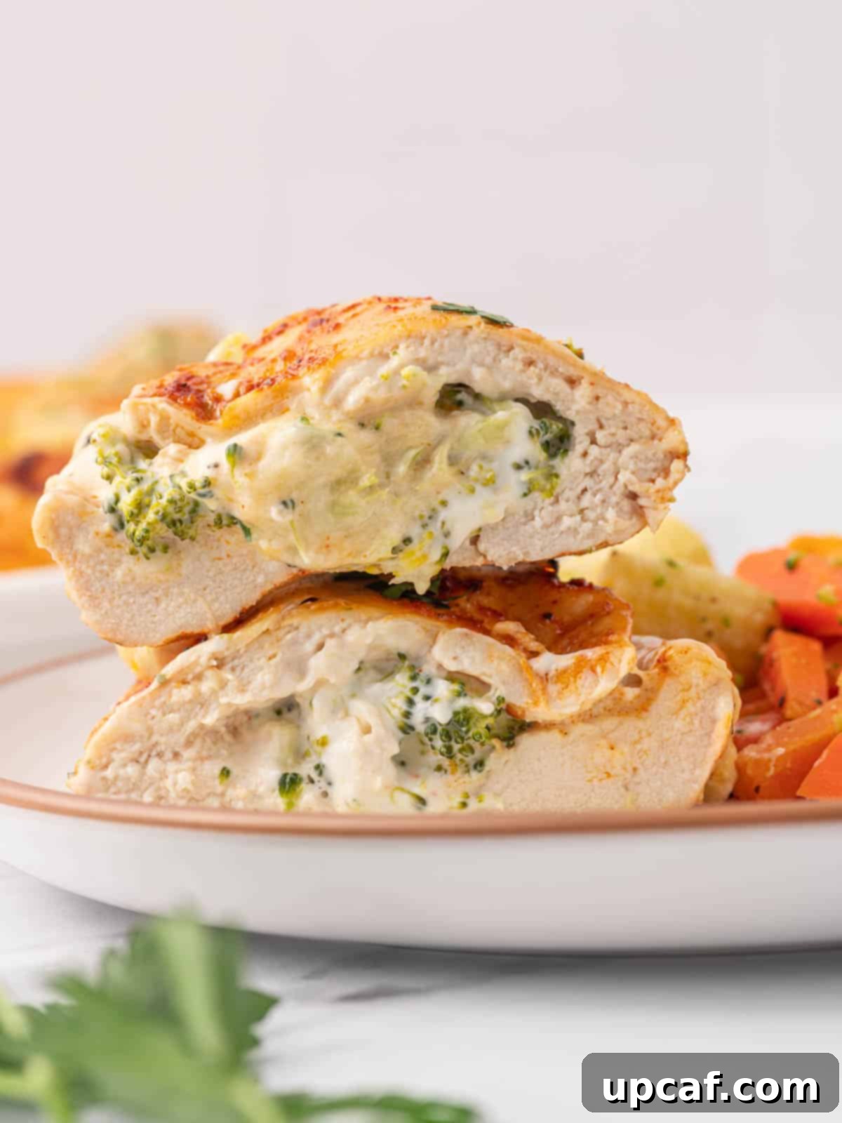 A broccoli stuffed chicken breast is cut in half on a plate, showcasing the creamy filling.