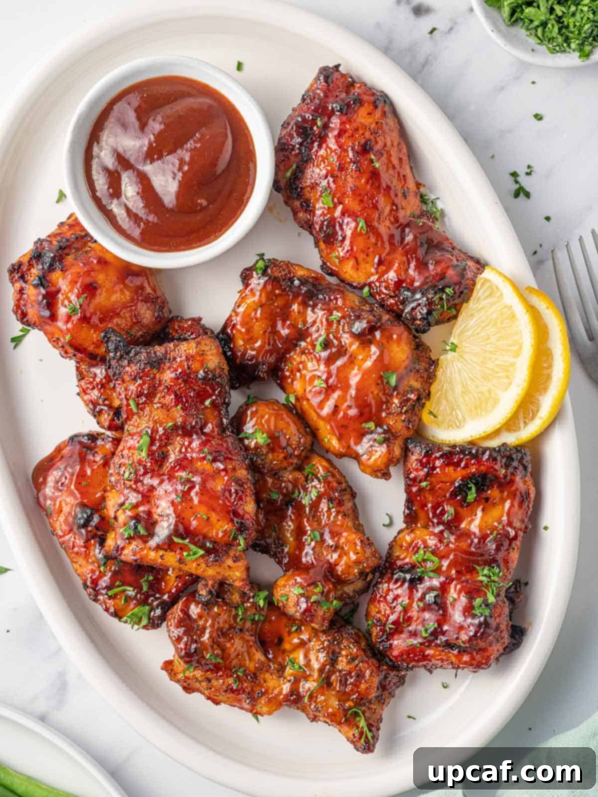 Air fryer bbq chicken on a plate with extra barbecue sauce, garnished with fresh parsley.