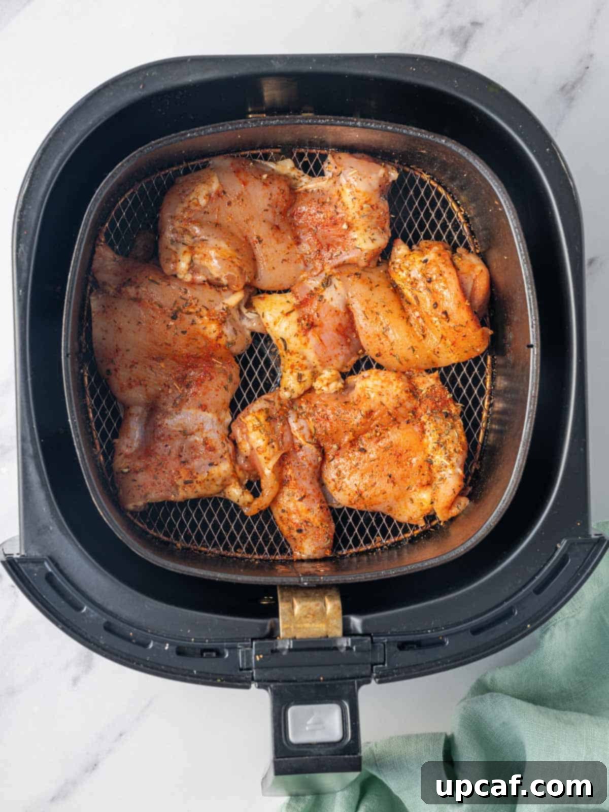 Chicken thighs seasoned and ready to be cooked in the air fryer basket.