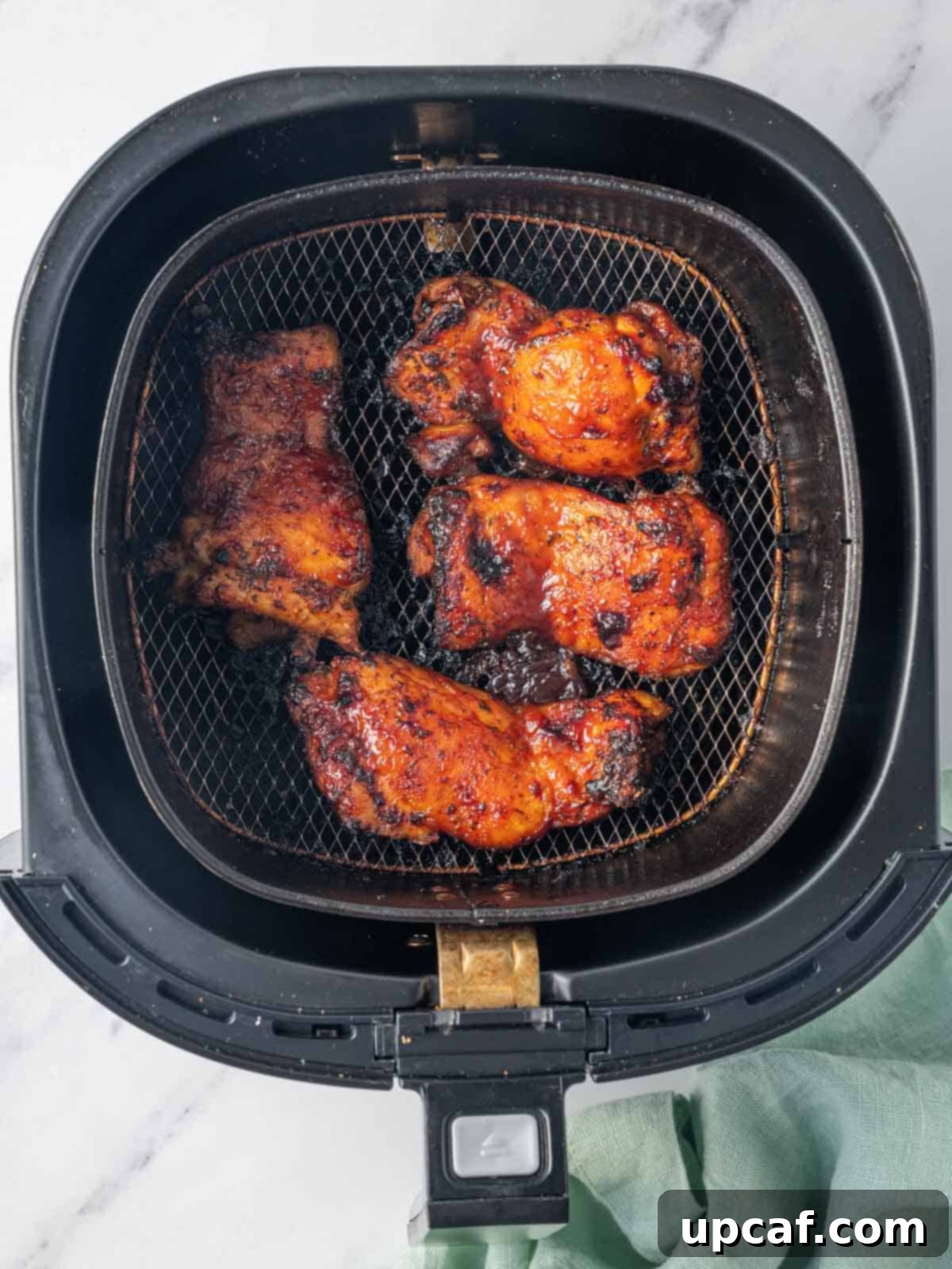 Finished bbq chicken thighs resting in an air fryer basket after cooking.