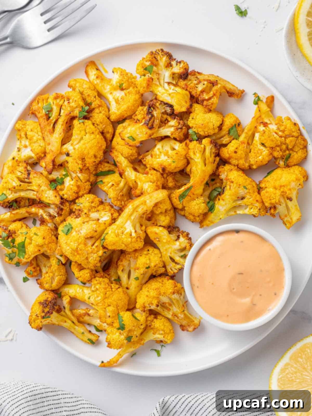 Golden brown air fryer cauliflower bites arranged on a tray, served with a creamy dipping sauce.