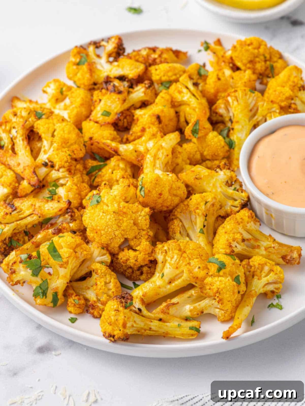 A beautifully plated dish of air fried cauliflower bites, garnished with fresh cilantro and served with a small bowl of dipping sauce and lemon wedges.