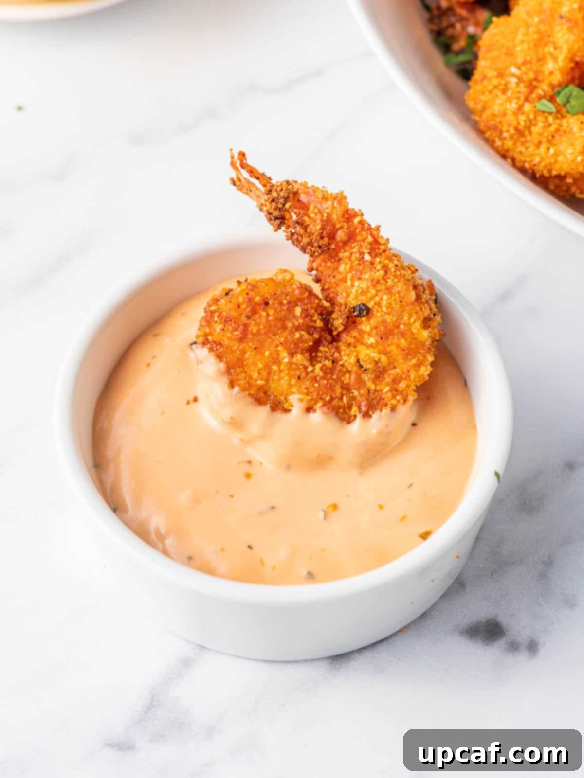 A bowl of dip with a keto breaded shrimp.