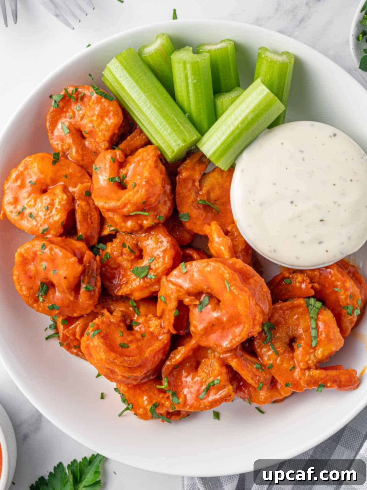 A plate of spicy fried buffalo shrimp served with a side of creamy dressing and celery sticks.