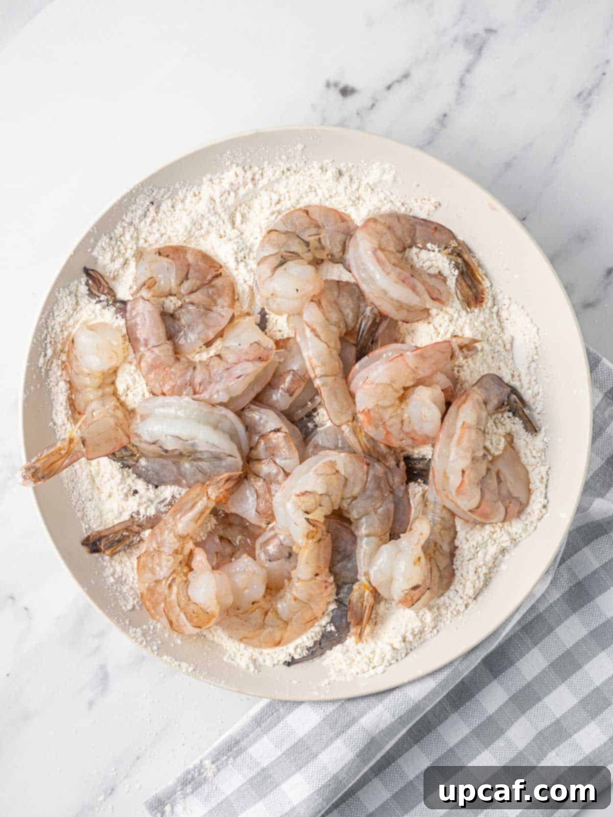 A close-up view of raw shrimp being coated in a seasoned flour mixture for pan frying.