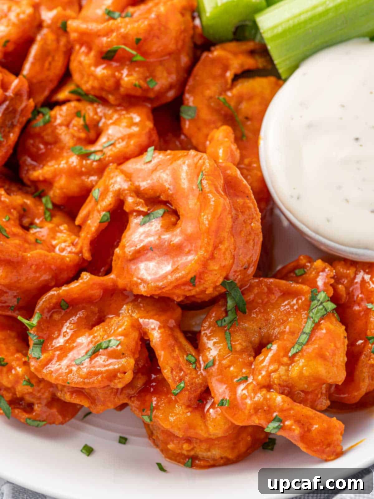 A close-up of spicy fried buffalo shrimp on a plate, garnished with parsley, with a small bowl of creamy dip in the background.