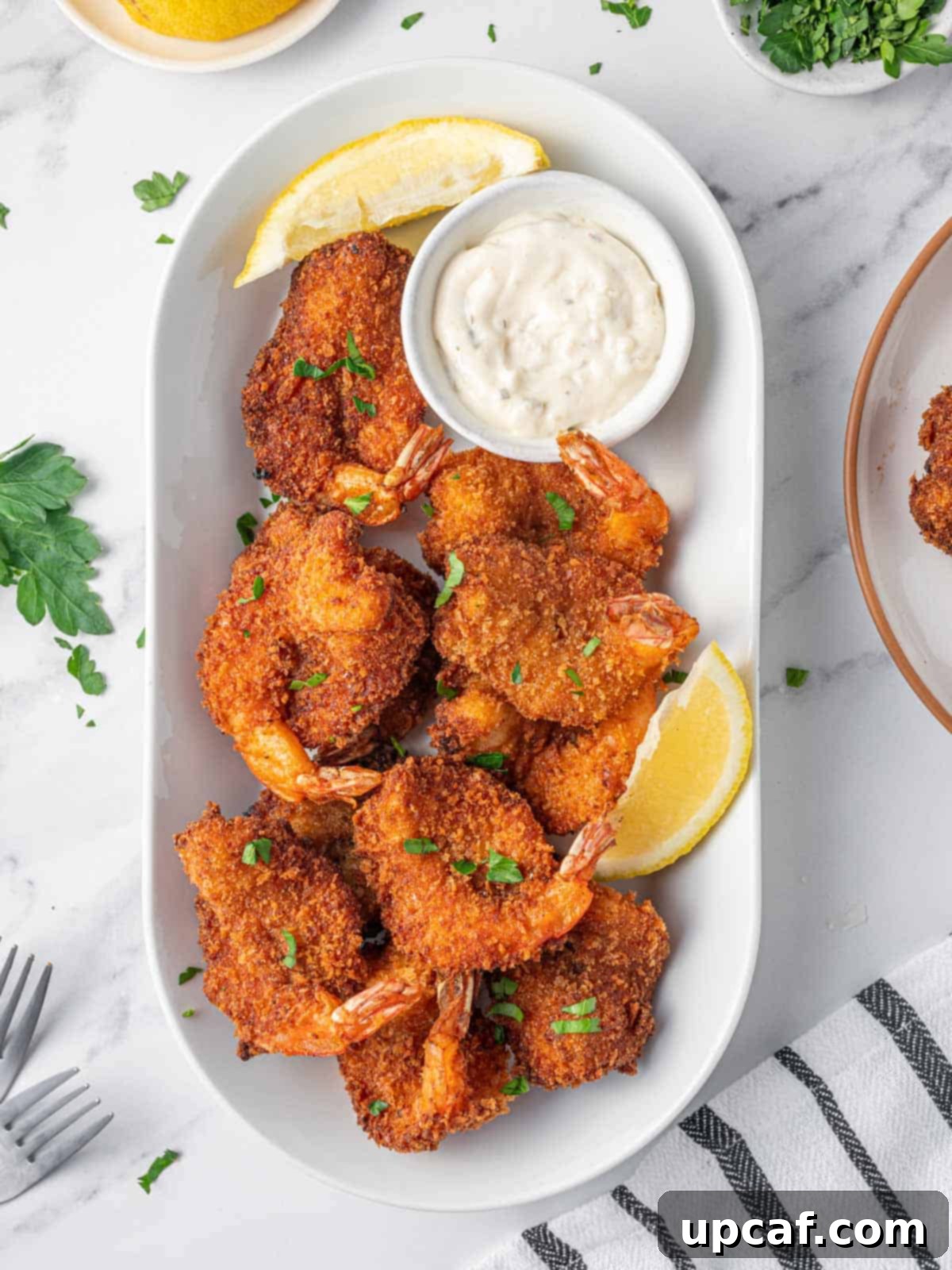 Fried butterfly shrimp on a platter with lemon wedges and tarter sauce.