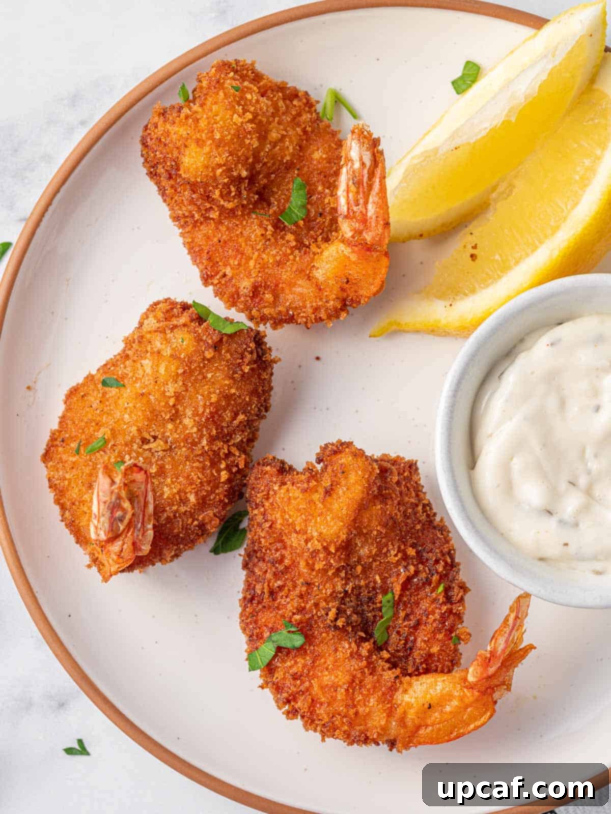 Three pan fried butterfly shrimp on a plate with tarter sauce.